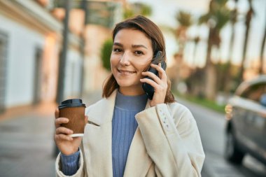 Genç İspanyol kadın akıllı telefondan konuşuyor ve şehirde kahve içiyor..