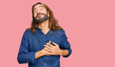 Uzun saçlı, sakallı, sıradan kıyafetler giyen, göğsünde elleri kapalı, yüzünde minnet ifadesi olan çekici bir adam. sağlık kavramı. 