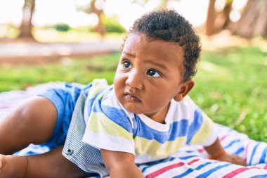 Sevimli Afro-Amerikan çocuk parkta çimlerin üzerinde oturuyor..