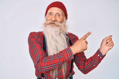 Gri saçlı, uzun sakallı, hippi görünümlü, yün şapkalı, gülümseyen ve kameraya bakan yaşlı bir adam.. 