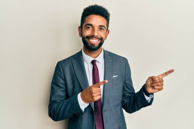 Yakışıklı, sakallı, takım elbiseli, kravatlı, gülümseyen ve kameraya bakan iki eli ve parmakları yanda olan bir adam.. 