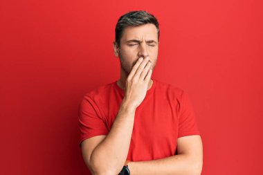 Gündelik kırmızı tişört giyen yakışıklı beyaz adam ağzıyla esnemekten sıkılmış. Huzursuz ve uykulu.. 