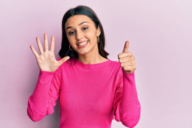 Genç İspanyol kadın gündelik giysiler giyiyor. Altıncı parmaklarını gösterip işaret ederken kendinden emin ve mutlu bir şekilde gülümsüyor.. 