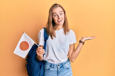 Güzel sarışın değişim öğrencisi elinde japan bayrağı tutarak başarıyı mutlu bir gülümsemeyle ve kazanan yüz ifadesiyle kutluyor. 