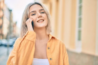 Genç sarışın kız gülümsüyor. Şehirdeki akıllı telefondan konuşuyor..