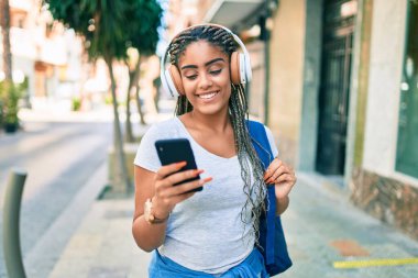 Genç Afrikalı Amerikalı öğrenci kampüste akıllı telefon kullanarak mutlu bir şekilde gülümsüyor.