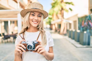 Beyaz tenli genç turist kız şehrin caddesinde klasik kamera kullanarak mutlu bir şekilde gülümsüyor..