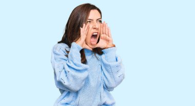 Kış süveteri giyen genç esmer kadın elleri ağzında kızgın bir şekilde bağırıyor. 