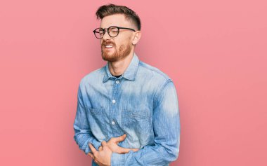 Genç, kızıl saçlı bir adam, eli karnında sıradan bir kot gömlek giyiyor çünkü mide bulantısı, acı verici bir hastalık kendini iyi hissetmiyor. Ağrı kavramı. 