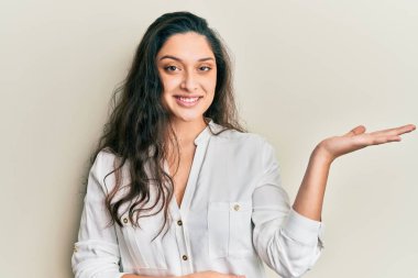 Güzel bir ortadoğulu kadın günlük kıyafetler giymiş neşeli bir şekilde gülümsüyor ve avuç içi kameraya bakıyor.. 