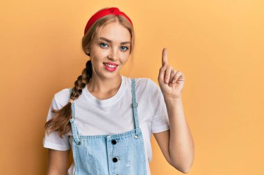 Güzel sarışın, beyaz kadın, günlük tulum giyip gülümsüyor bir fikir veya soruyla, mutlu bir yüzle işaret ederek, bir numara. 