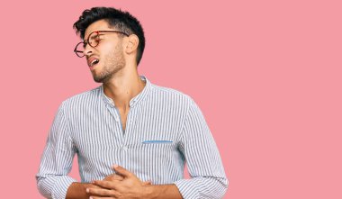 Genç yakışıklı bir adam günlük kıyafetler giyiyor ve elleri karnında gözlük takıyor çünkü mide bulantısı, acı verici bir hastalık kendini iyi hissetmiyor. Ağrı kavramı. 