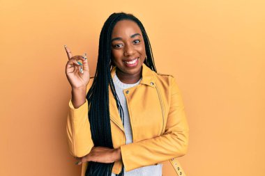 Genç Afro-Amerikalı kadın, sıradan bir ceket giyiyor. Yüzünde kocaman bir gülümseme var. Elleri ve parmaklarıyla kameraya bakıyor.. 