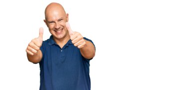 Orta yaşlı kel bir adam, günlük giysiler giyip, olumlu jestler yapıyor, gülümsüyor ve başarı için seviniyor. kazanan jest. 