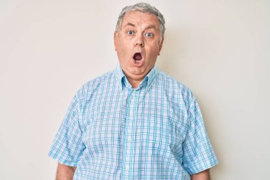 Kıdemli, gri saçlı, günlük kıyafetler giyen, ağzı açık, korkmuş ve şaşırmış bir adam. 