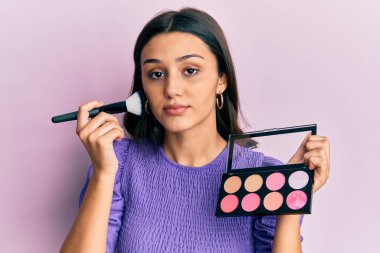 Makyaj fırçası tutan genç İspanyol kadın yüzünde ciddi bir ifadeyle rahatladı. Basit ve doğal bir şekilde kameraya bakıyorsun.. 