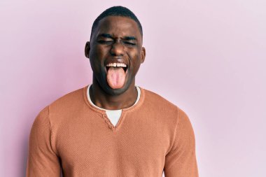 Genç, Afro-Amerikan bir adam günlük kıyafetler giyiyor. Dilini komik bir ifadeyle dışarı çıkarıyor. duygu kavramı. 