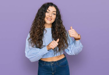 Gündelik giysiler giyen genç İspanyol kız arka tarafı işaret ediyor. Elleri havada, kendinden emin gülümsüyor. 