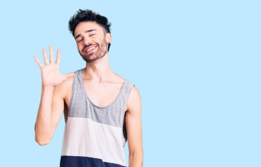 Gündelik kıyafetler giyen genç İspanyol adam beş numarayı gösterip işaret ederken kendinden emin ve mutlu bir şekilde gülümsüyor.. 