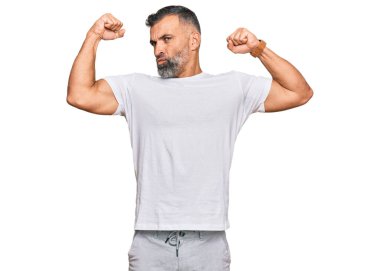 Orta yaşlı beyaz tişört giyen yakışıklı adam gururla gülümseyen kol kaslarını gösteriyor. fitness konsepti. 