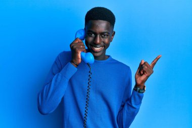 Genç Afro-Amerikan adam elinde klasik bir telefonla gülümsüyor mutlu bir şekilde el ve parmak kenarı işaret ediyor. 