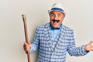 Olgun orta doğulu bıyıklı adam klasik ve zarif moda tarzıyla başarıyı mutlu bir gülümsemeyle kutluyor ve kazanan el kaldırarak ifade ediyor. 