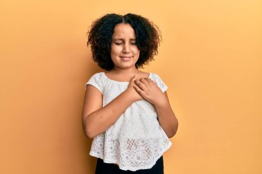 Afro saçlı, sıradan kıyafetler giyen, göğsünde elleri kapalı, yüzünde minnet ifadesi olan genç bir kız. sağlık kavramı. 