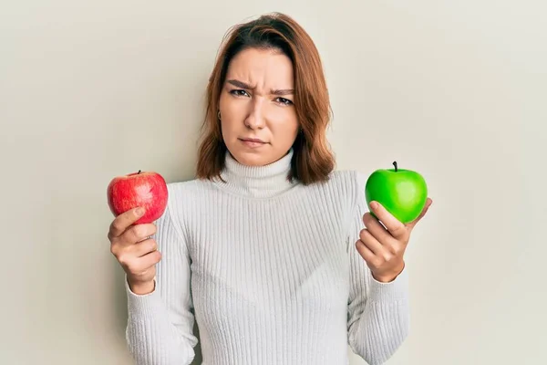 年轻的高加索女人 手里拿着红绿相间的苹果 毫无头绪 面目全非 怀疑概念 — 图库照片