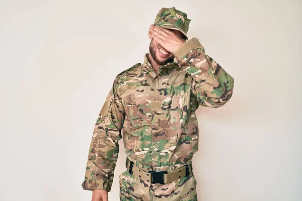 カモフラージュ軍の制服を着た若い白人男性が笑顔で 驚きのために目を覆う顔を手で笑っています 視覚障害の概念 — ストック写真