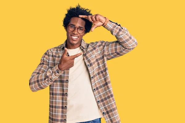 アフロの髪をしたハンサムなアフリカ系アメリカ人男性は カジュアルな服と眼鏡を着て 幸せな顔をした手と指でフレームを作って笑っています 創造性と写真の概念 — ストック写真