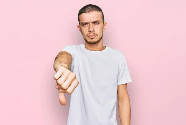 カジュアルな白いTシャツを着たヒスパニック系の若者は 親指を下にジェスチャーで拒絶と否定を示す不満と怒りを見ています 悪い表現 — ストック写真