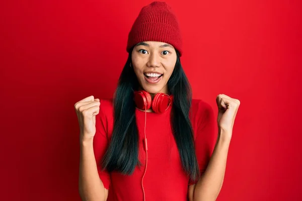 年轻的中国女人一边听音乐一边用耳机庆祝成功 惊讶地举起双臂睁开眼睛 获奖者概念 — 图库照片