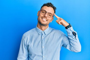 Gündelik kıyafetler ve gözlük takan genç İspanyol bir adam tek parmakla kafasını işaret ediyor, harika bir fikir ya da düşünce, iyi bir hafıza. 