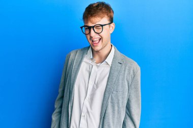 Zarif kıyafetler giyen ve gözlüklü genç beyaz adam kameraya seksi bir ifadeyle bakıyor, neşeli ve mutlu bir yüzle.. 