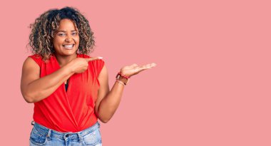 Genç Afro-Amerikan artı cüsseli kadın kolsuz gömlekli gündelik tarzda giyiniyor kameraya hayret ediyor ve gülümsüyor.. 