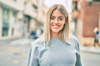 Genç sarışın kız gülümsüyor, mutlu bir şekilde şehirde duruyor..