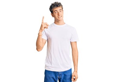 Gündelik beyaz t-shirt giyen genç yakışıklı adam başarılı bir fikri işaret ediyor. Heyecanlı ve mutlu. Bir numara.. 