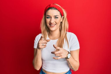 Gündelik beyaz tişört giyen genç beyaz kadın mutlu ve komik yüzüyle kamerayı işaret ediyor. iyi enerji ve titreşimler. 