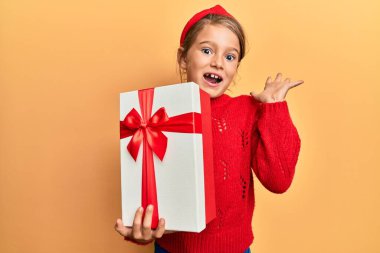 Küçük güzel kız başarıyı kutlamak için hediyesini tutarken mutlu bir gülümseme ve kaldırılmış bir el ile kazanan bir ifade. 