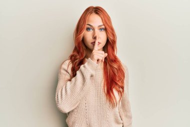 Genç, güzel, kızıl saçlı, sıradan bir kazak giyen ve parmakları dudaklarında sessiz olmak isteyen bir kadın. sessizlik ve gizli konsept. 