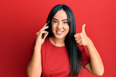 Genç ve güzel İspanyol kız akıllı telefonda konuşuyor mutlu ve olumlu gülümsüyor, başparmağıyla mükemmel ve onay işareti yapıyor. 
