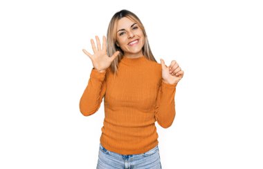 Gündelik giysiler giyen genç beyaz kadın altı numarayı gösterip işaret ederken kendinden emin ve mutlu gülümsüyor.. 