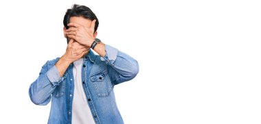 Gündelik kıyafetler giyen genç İspanyol adam gözlerini ve ağzını elleriyle kapatıyor, şaşırmış ve şok olmuş. duygu gizleme 