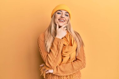 Kışlık yün kazak ve şapka giyen genç beyaz kadın kameraya kendinden emin bakıyor kollarını kavuşturmuş ve çenesini kaldırmış gülümsüyor. Olumlu düşünmek. 