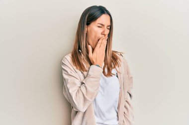 Esmer, gündelik kıyafetler giyen genç bir kadın ağzıyla ağzını kapatmaktan sıkılmış. Huzursuz ve uykulu.. 