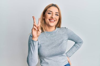 Gündelik giysiler giyen genç beyaz kadın iki numarayı gösterip işaret ederken kendine güvenen ve mutlu bir şekilde gülümsüyor.. 