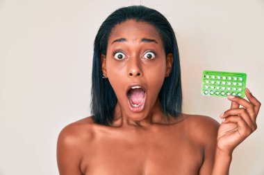 Genç Afro-Amerikalı kadın elinde doğum kontrol hapları tutuyor. Çılgınca ve şaşkınlıkla kutluyor. Gözleri açık, heyecanla haykırıyor.. 