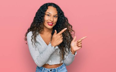 Kıvırcık saçlı, sıradan giyinmiş, gülümseyen ve kameraya bakan iki eli ve parmakları yandan gösteren genç İspanyol kadın.. 