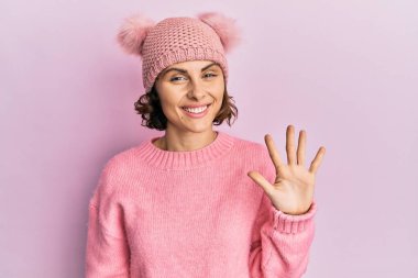 Şirin yün şapkalı genç esmer kadın beş numarayı gösterip işaret ederken kendinden emin ve mutlu bir şekilde gülümsüyor.. 