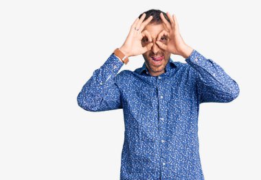 Sıradan kıyafetler giyen genç yakışıklı bir adam dürbün gibi jest yapıyor. Dürbün dilini çıkarıyor, gözler parmaklarından bakıyor. çılgın ifade. 